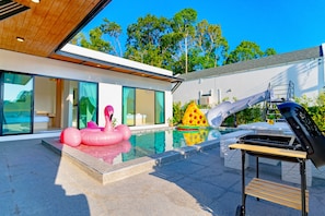 Enjoy a refreshing swim in the pool surrounded by a deck and barbecue grill, with a view of the lush surroundings.