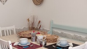 Un coin repas avec une table dressée pour quatre personnes, des chaises blanches avec des coussins bleus, un set de table en fibres tressées, une assiette décorative et un panier tressé fixé au mur.