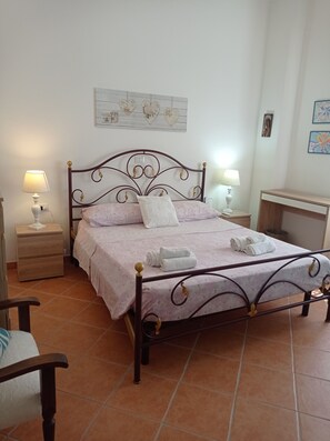 A neatly made bed with a floral bedspread, two pillows, and rolled towels on a metal frame bed in a room with tiled flooring.