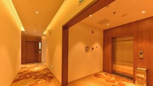 A hotel corridor with wooden flooring, an elevator, and a door at the end. - James Joyce Coffetel (Beijing Happy Valley Fatou Metro Station) (Beijing)