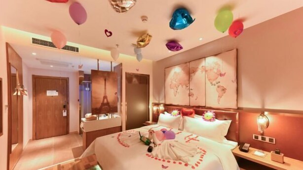 A hotel room with a large bed, a nightstand, a mirror, and a wall with a world map. - James Joyce Coffetel (Beijing Happy Valley Fatou Metro Station) (Beijing)