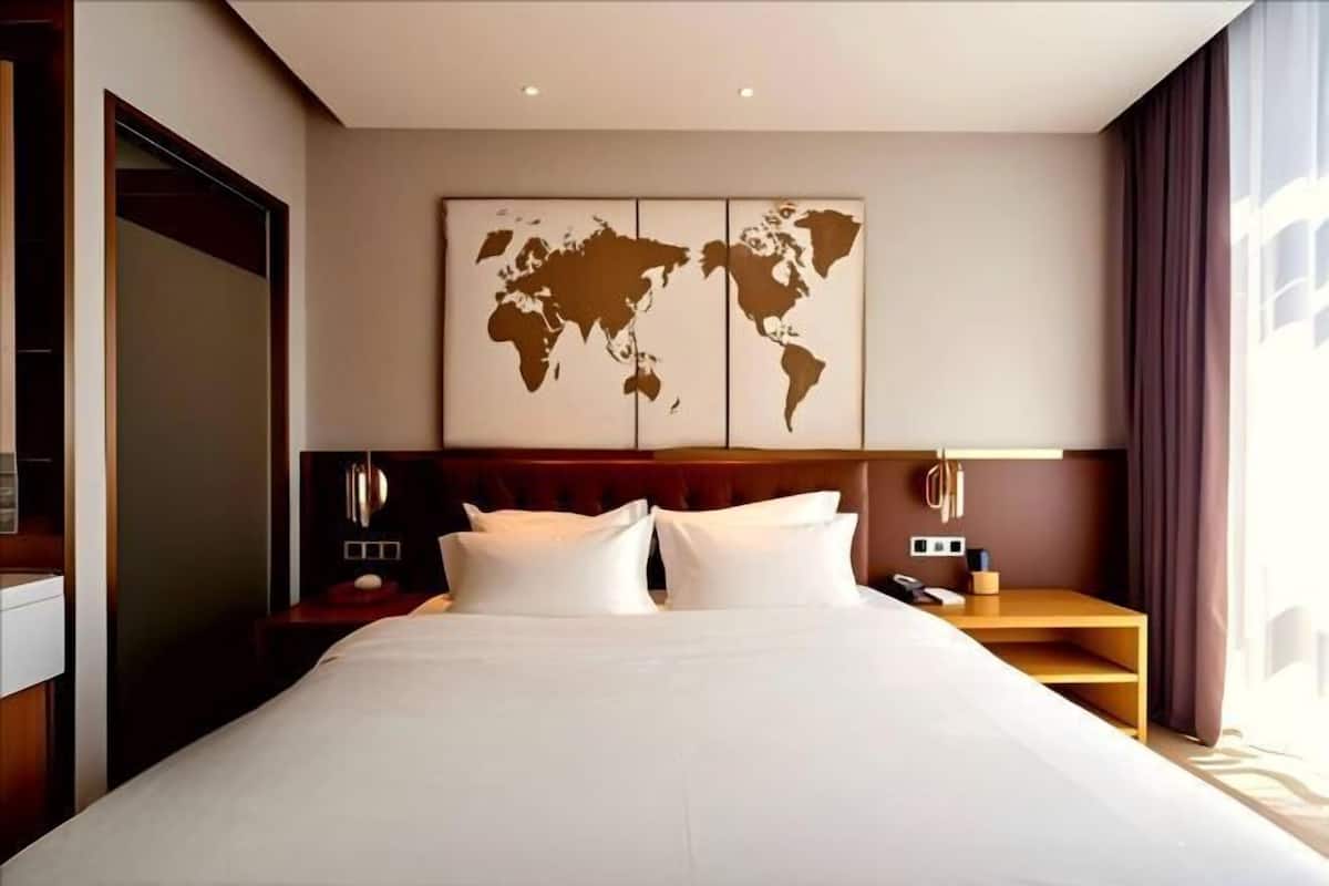 Une chambre d’hôtel avec un grand lit, une carte du monde accrochée au mur, un bureau avec une lampe et une fenêtre avec des rideaux.