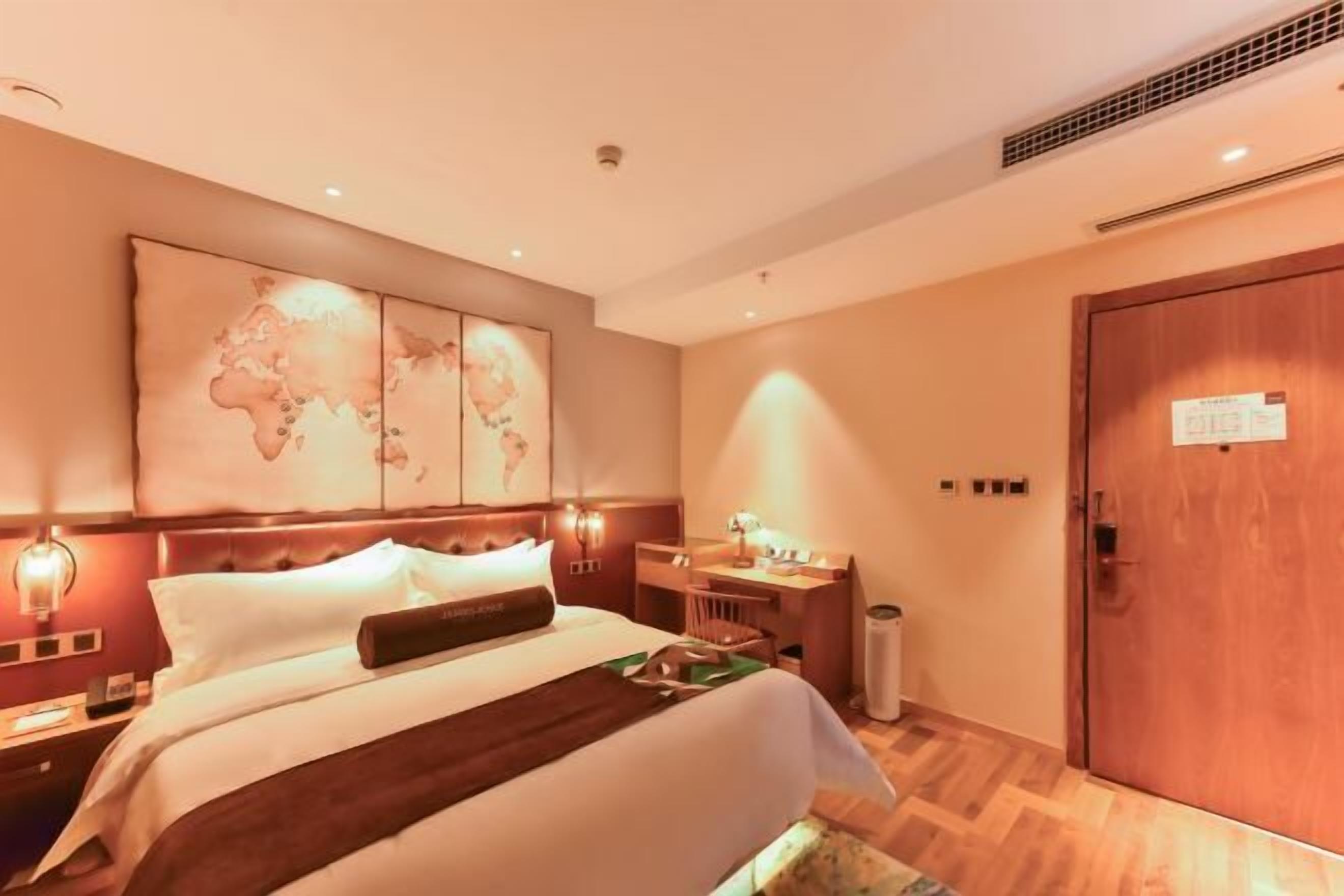 A hotel room with a large bed, a desk, and a world map on the wall.