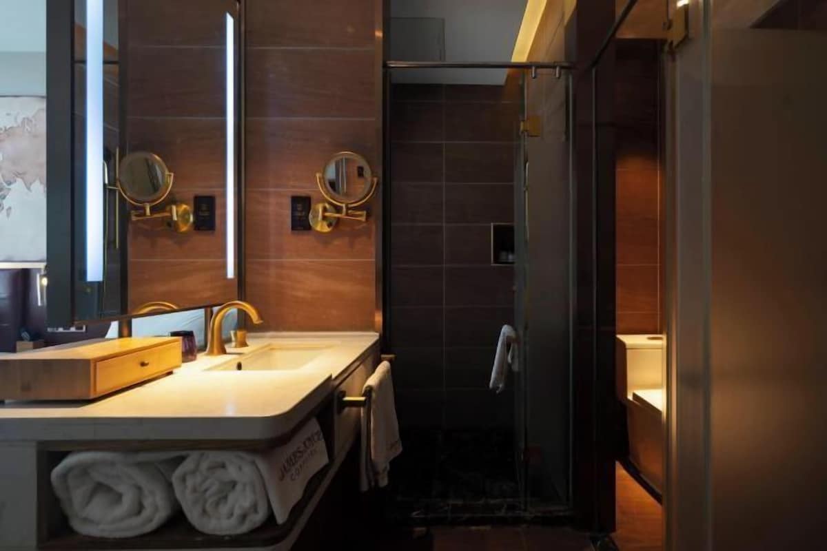 A modern bathroom with a dual sink vanity, two wall-mounted mirrors, a towel rack, and a glass shower enclosure.