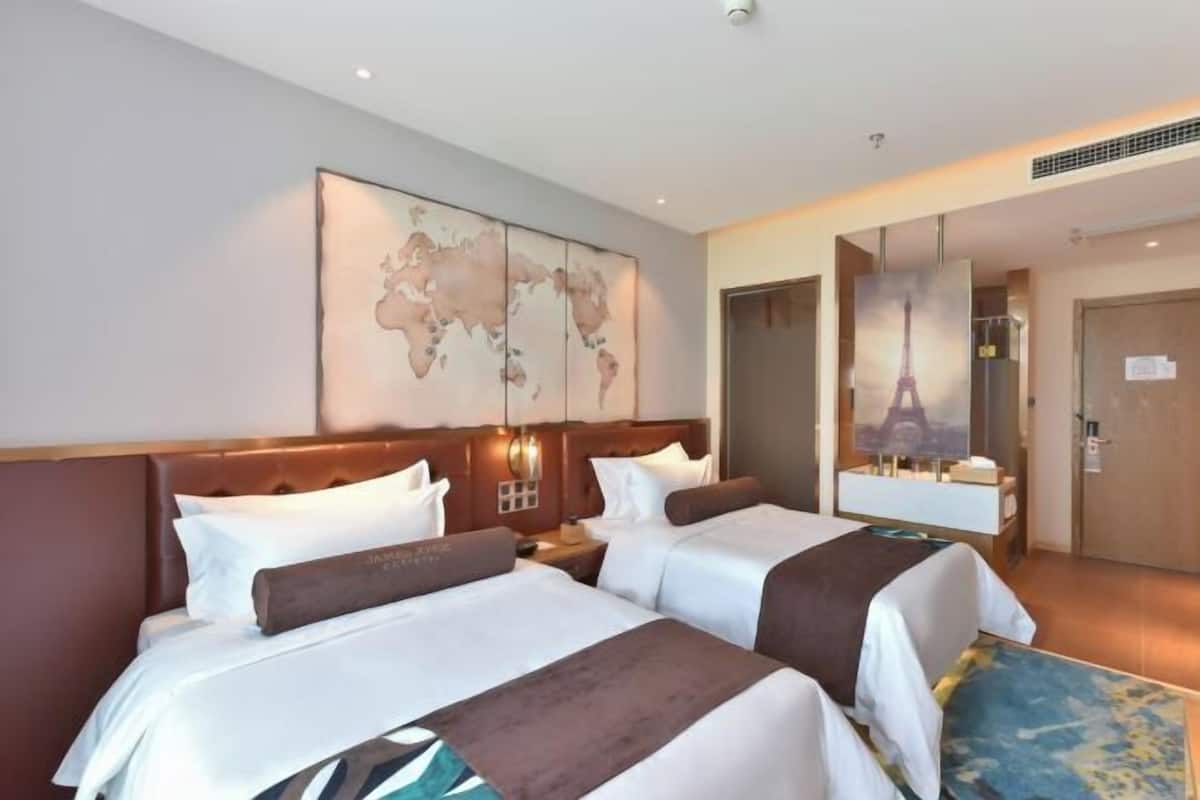 Une chambre d’hôtel avec deux lits, une carte du monde accrochée au mur, un grand miroir et une porte ornée d’une image de la Tour Eiffel.