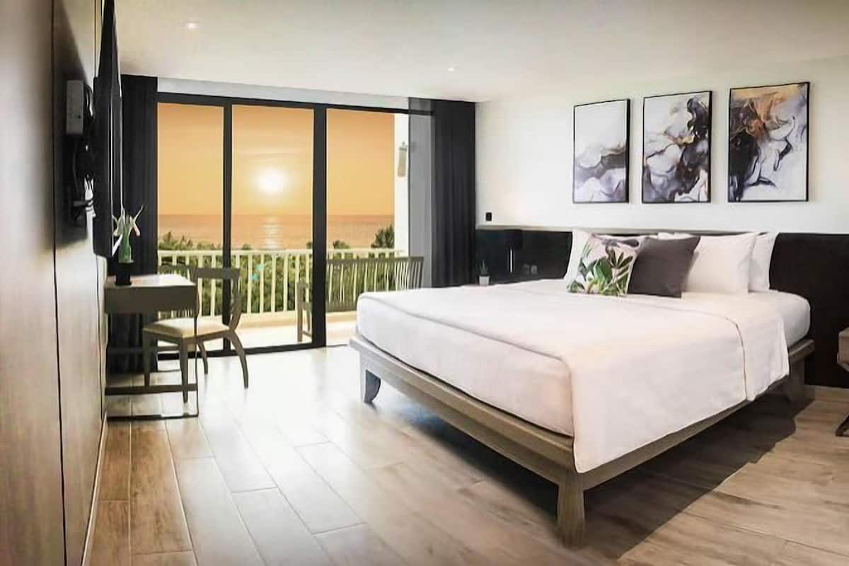 Un dormitorio con cama, escritorio y silla, un balcón con vistas, y tres obras de arte en la pared.
