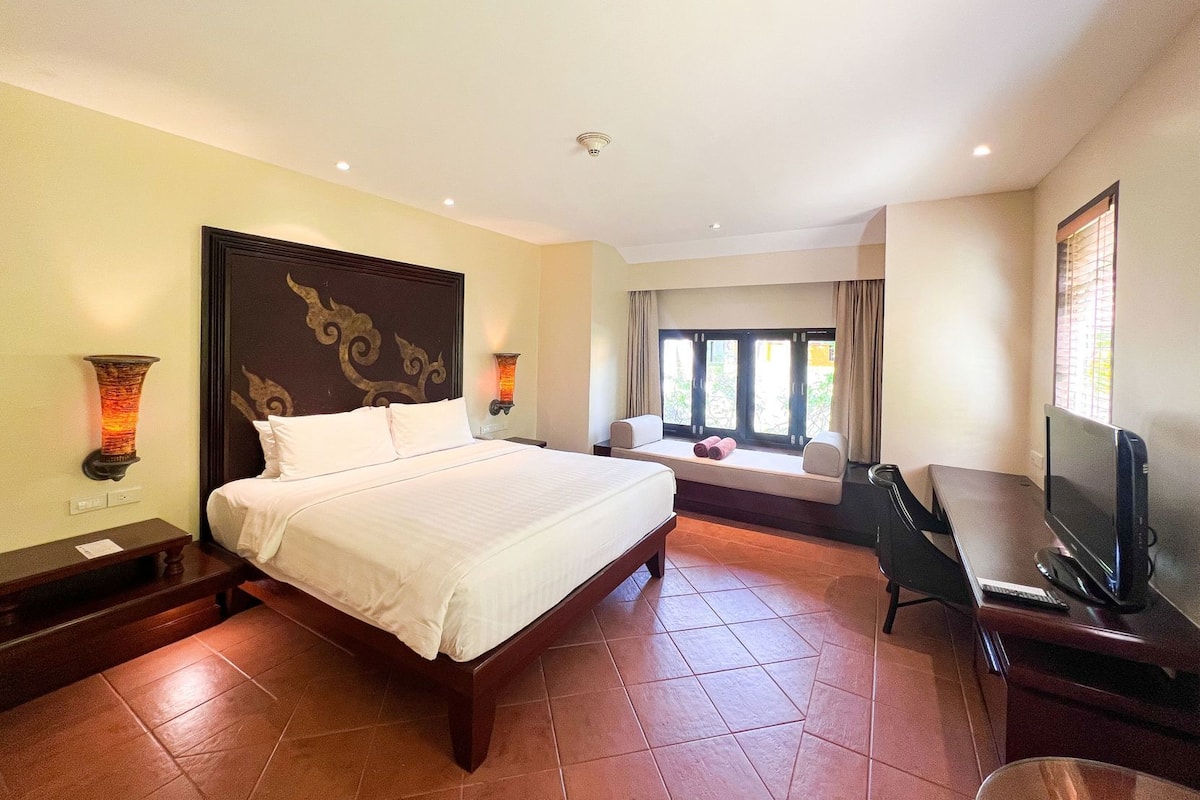 Una habitación de hotel con una cama grande, un escritorio con televisor y una ventana con cortinas.