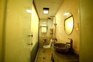 A compact bathroom with a glass shower enclosure, a toilet, and a large stone sink with a mirror above it. - Riverside Inn (Shimian)