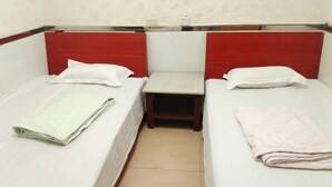 A room with two single beds, each with a pillow and a folded blanket. There is a small table between the beds. - Yuqi Hostel (Chongqing)