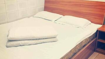 A bed with a wooden headboard, white bedding, and a wooden nightstand beside it.