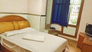 A neatly made bed with white linens and pillows, a wooden headboard, a small bedside table with a television, and a window with blue curtains. - Yuqi Hostel (Chongqing)