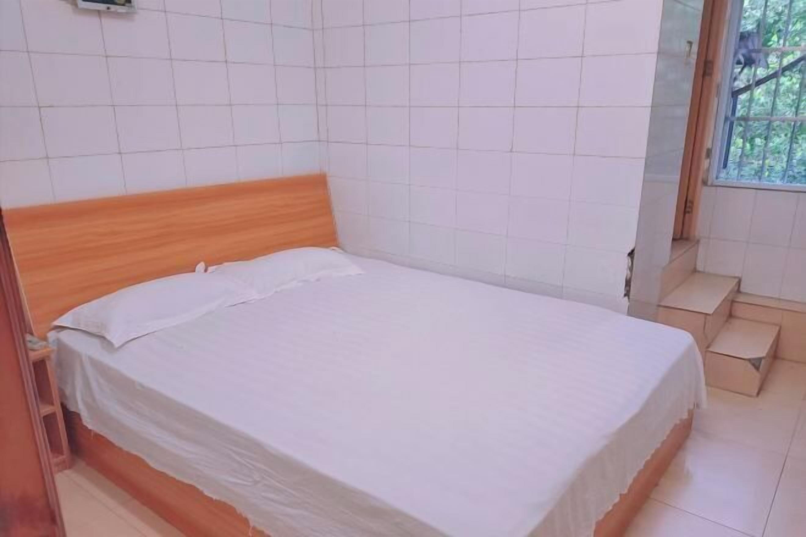 A single bed with a wooden headboard in a room with white tiled walls and a window with a view of greenery.