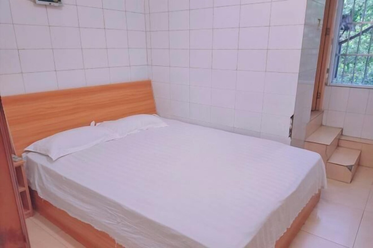 A single bed with a wooden headboard in a room with white tiled walls and a window with a view of greenery.