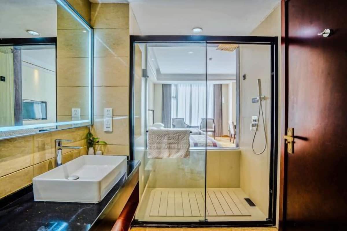 Une salle de bain moderne avec un grand miroir, un lavabo blanc et une douche séparée par des parois en verre.