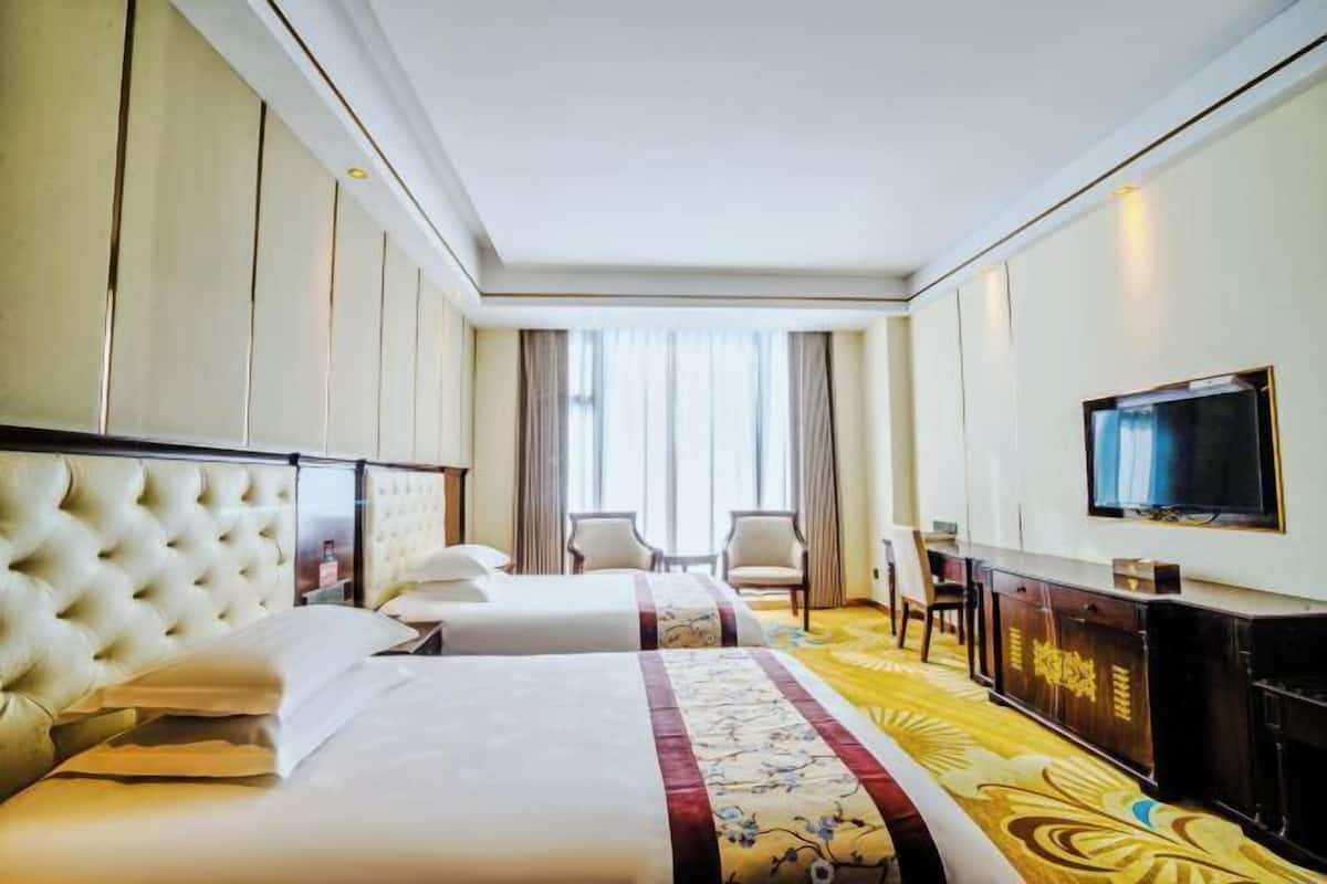 Une chambre d’hôtel avec deux lits, une télévision, un bureau et une grande fenêtre.