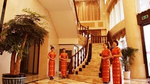 A grand lobby with a marble staircase, large potted plants, and a reception area with staff in traditional attire. - Xinghua Grand Hotel (Xinghua)