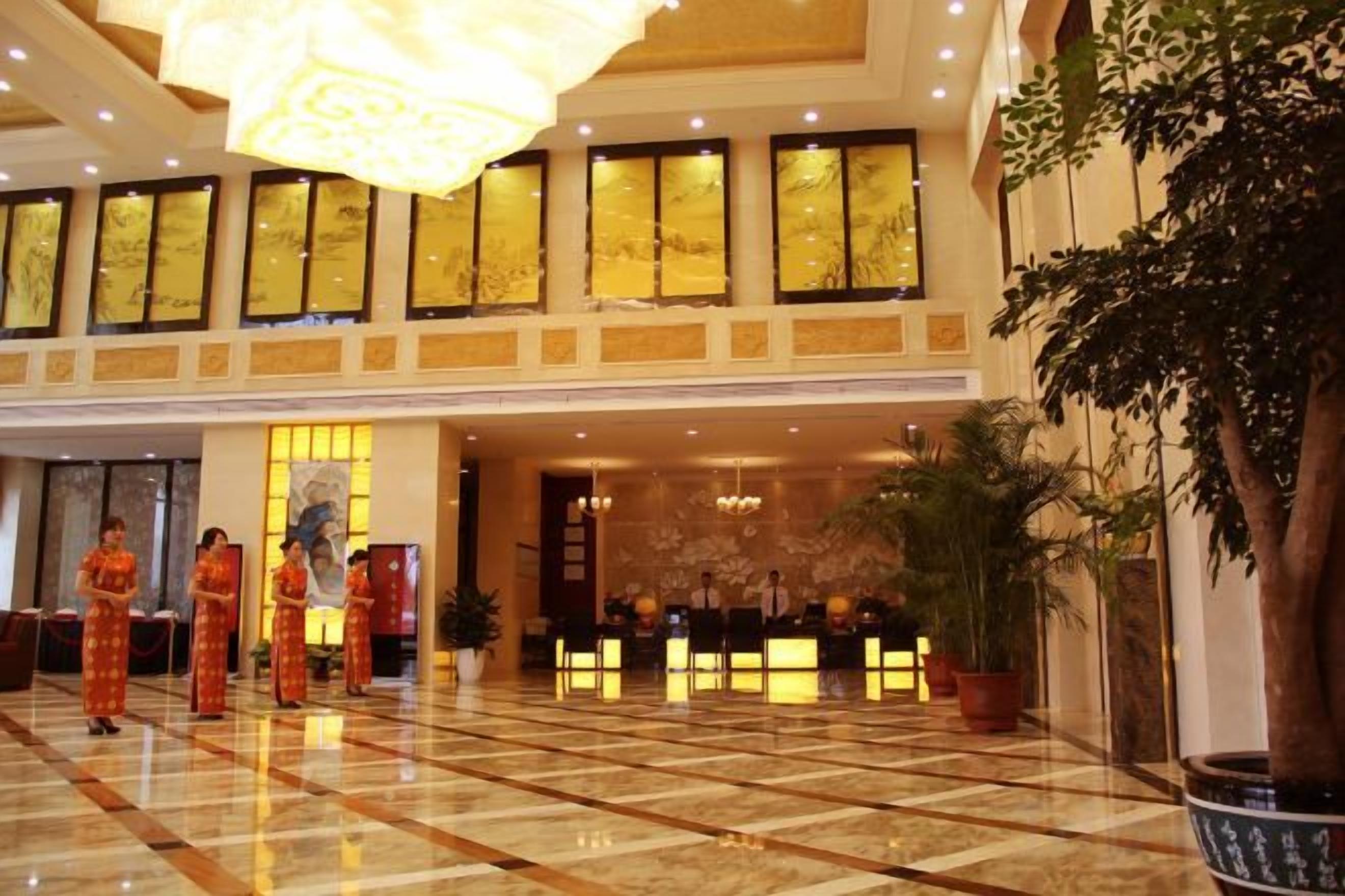 Un vestíbulo de hotel con una recepción, una lámpara de araña grande y un área de recepción con personal.