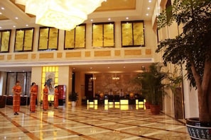 A hotel lobby with a reception desk, a large chandelier, and a reception area with staff.