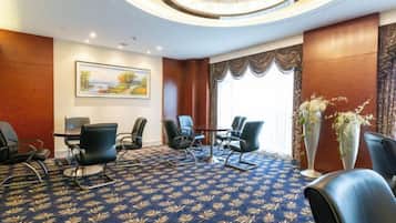 A conference room with a round table, multiple chairs, a patterned carpet, and a painting on the wall.