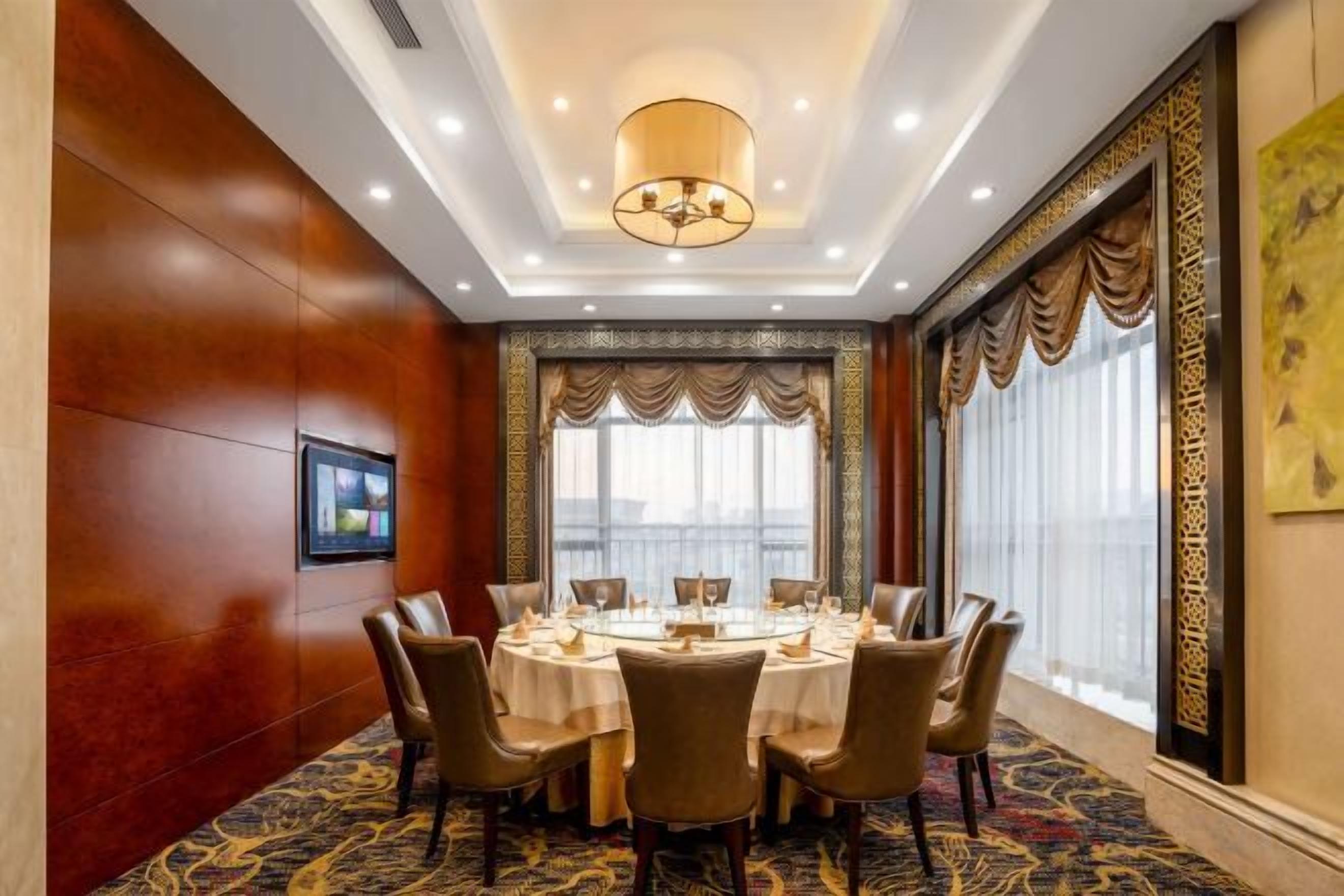 A conference room with a round table, chairs, and a large window with curtains.