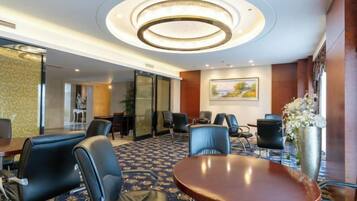 A hotel conference room with a round table, chairs, a large vase with flowers, and a painting on the wall.