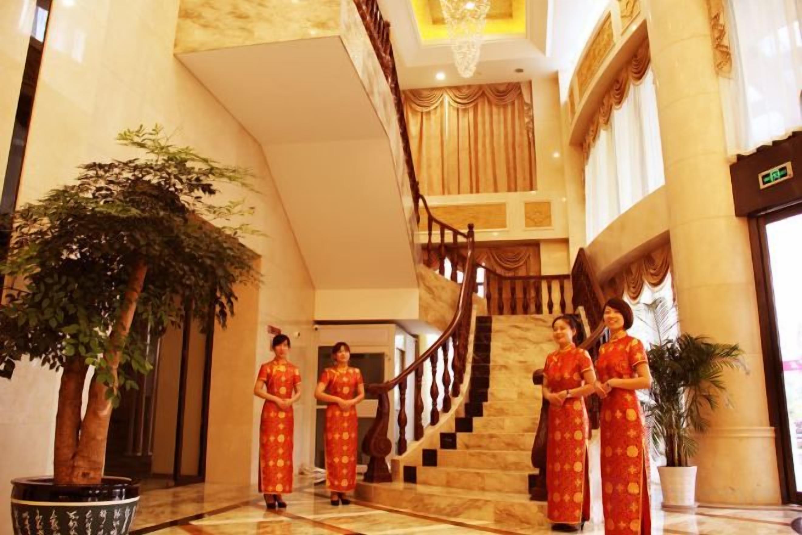 A grand lobby with a marble staircase, large potted plants, and a reception area.