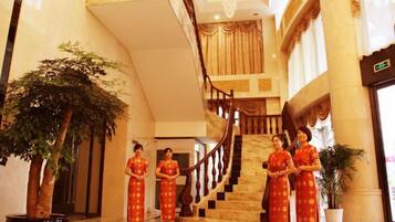 A grand lobby with a marble staircase, large potted plants, and a reception area.