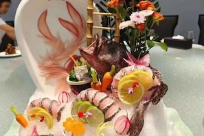 A table with a decorative centerpiece featuring a ceramic animal, flowers, and food items. - Xinghua Grand Hotel (Xinghua)