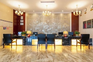 Zona de recepción de hotel con piso de mármol, mostradores negros y un gran mural floral.