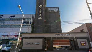 A building with a prominent 'MUHOTEL' sign on the facade, a large entrance with a garage door, and a parking sign indicating a parking area. - Sasang Hotel MU (Busan)