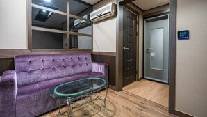 A room with a purple sofa, a glass table, an air conditioning unit, and a door with a control panel. - Sasang Hotel MU (Busan)