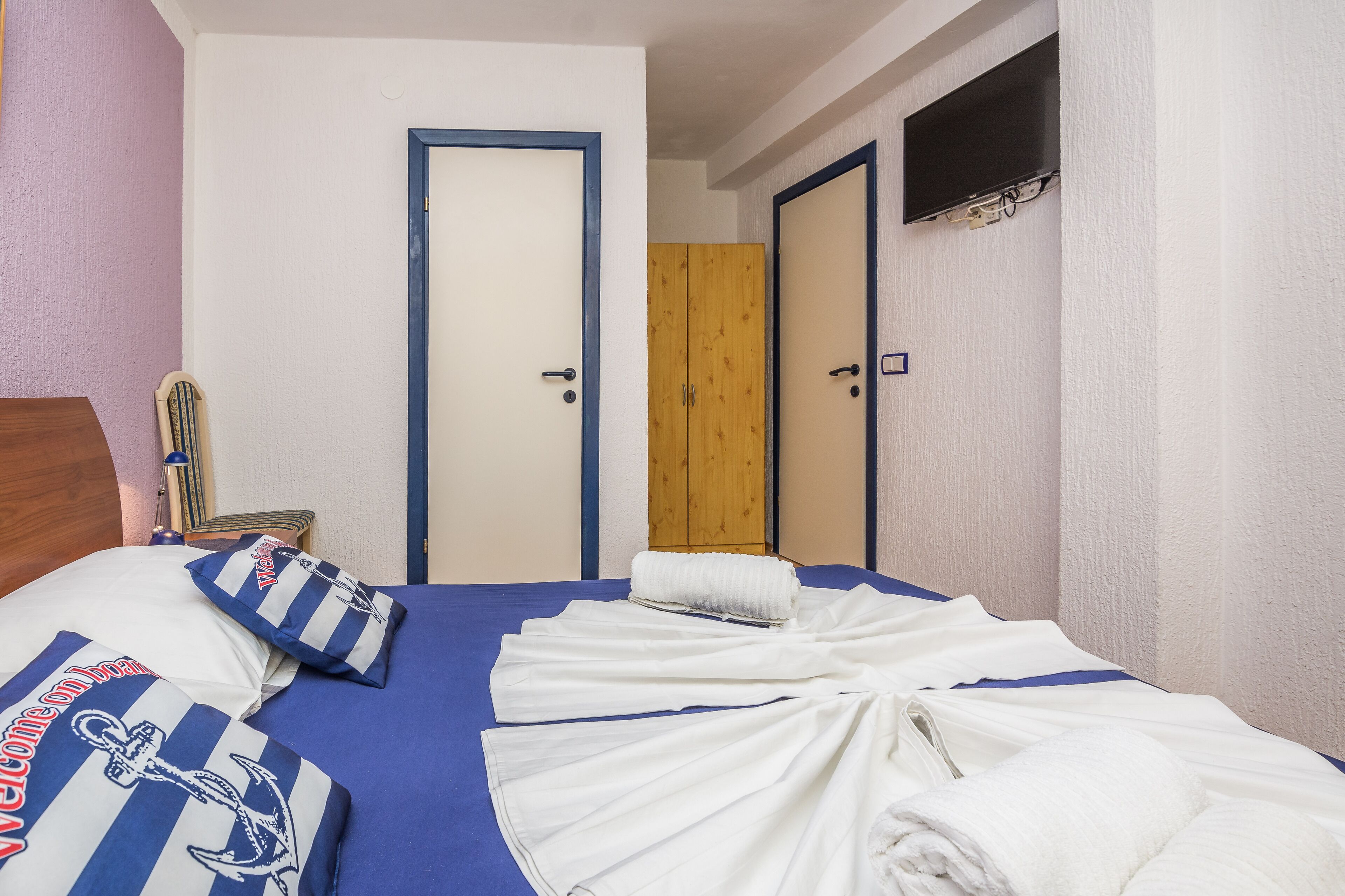 Habitación de hotel con una cama, un armario de madera y un televisor montado en la pared.