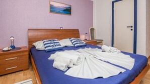 Ein ordentlich bezogenes Bett mit blauer Bettwäsche und weißen Handtüchern, ein Nachttisch aus Holz mit einer Lampe und ein Sonnenuntergangsbild an der Wand.