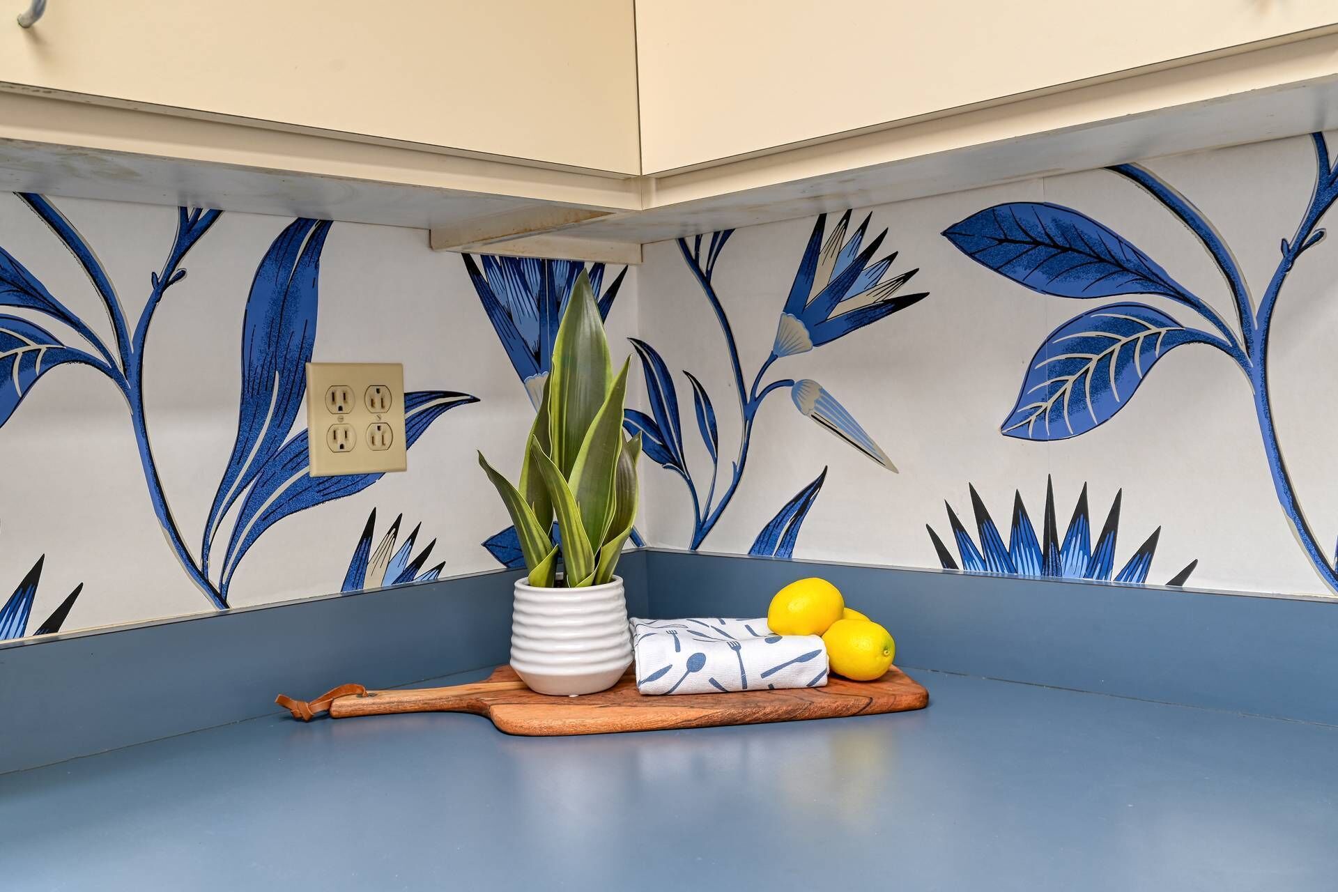 A kitchen corner with a blue countertop, a potted plant, a cutting board, and lemons.