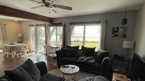 A modern living room with a black sofa, a round coffee table, and a television. There is a dining area with a table and chairs visible through a glass door.