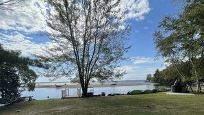 A grassy outdoor area with two lounge chairs facing a lake and a clear sky.