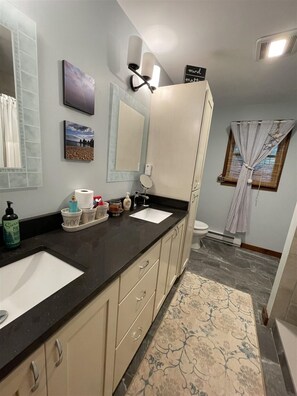 Une salle de bain avec deux lavabos, un miroir, un porte-serviettes et une fenêtre avec des rideaux.