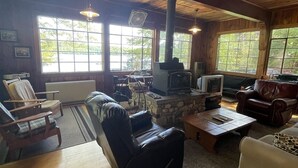 A cozy living room with a stone fireplace, leather sofas, and wooden flooring. - Highland Holiday Limit 7-10 3 Bedroom Cottage by RedAwning (Bridgton)