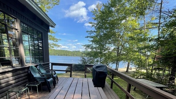A wooden deck with a picnic table and chairs, overlooking a lake. - Highland Holiday Limit 7-10 3 Bedroom Cottage by RedAwning (Bridgton)