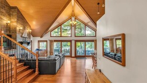 Amplia sala de estar con techos altos, una escalera de madera y grandes ventanales que ofrecen vistas al exterior.