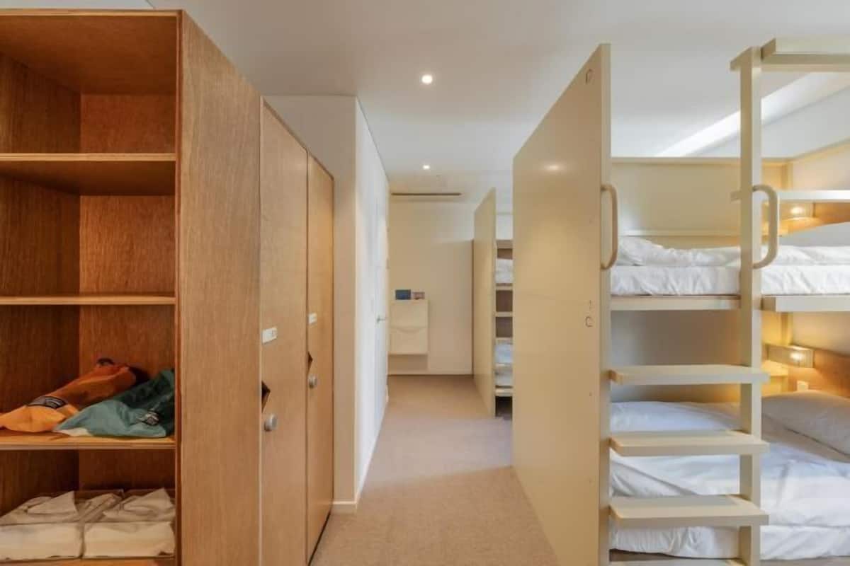 Une chambre avec des lits superposés, une armoire en bois et un sol recouvert de moquette.