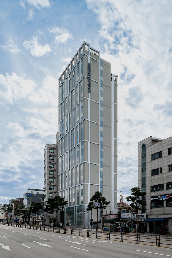 A modern multi-story hotel with a glass facade, located on a street with other buildings and trees.