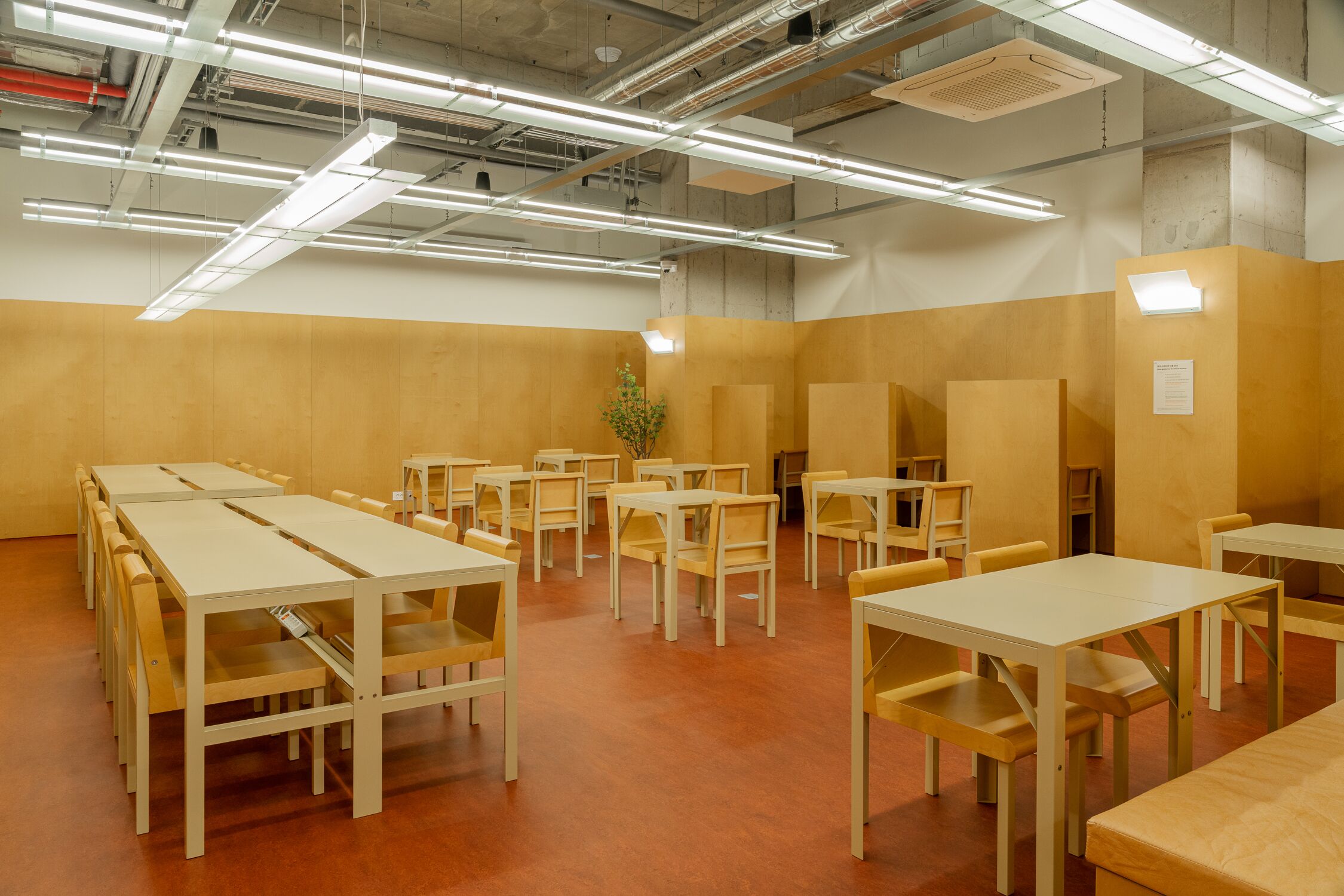 A conference room with multiple tables and chairs, high ceiling with exposed ductwork, and a wooden wall.