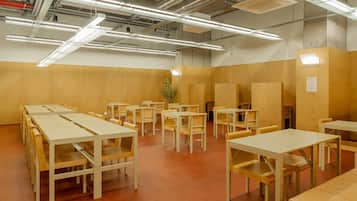 A conference room with multiple tables and chairs, high ceiling with exposed ductwork, and a wooden wall.