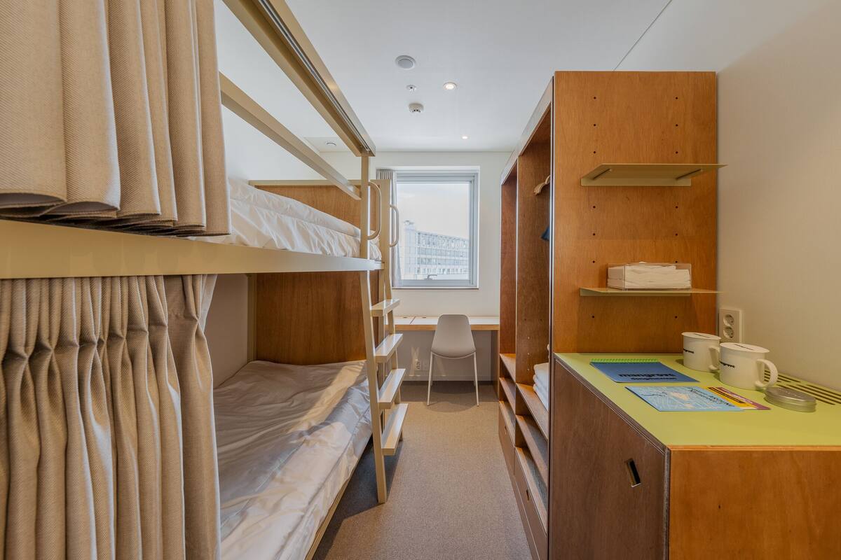 Une chambre d’hôtel compacte équipée de lits superposés, d’un bureau, d’une chaise et d’un petit coin cuisine.