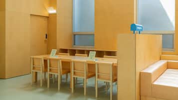 A room with a long wooden table and chairs, a small wooden desk, and a cushioned bench.