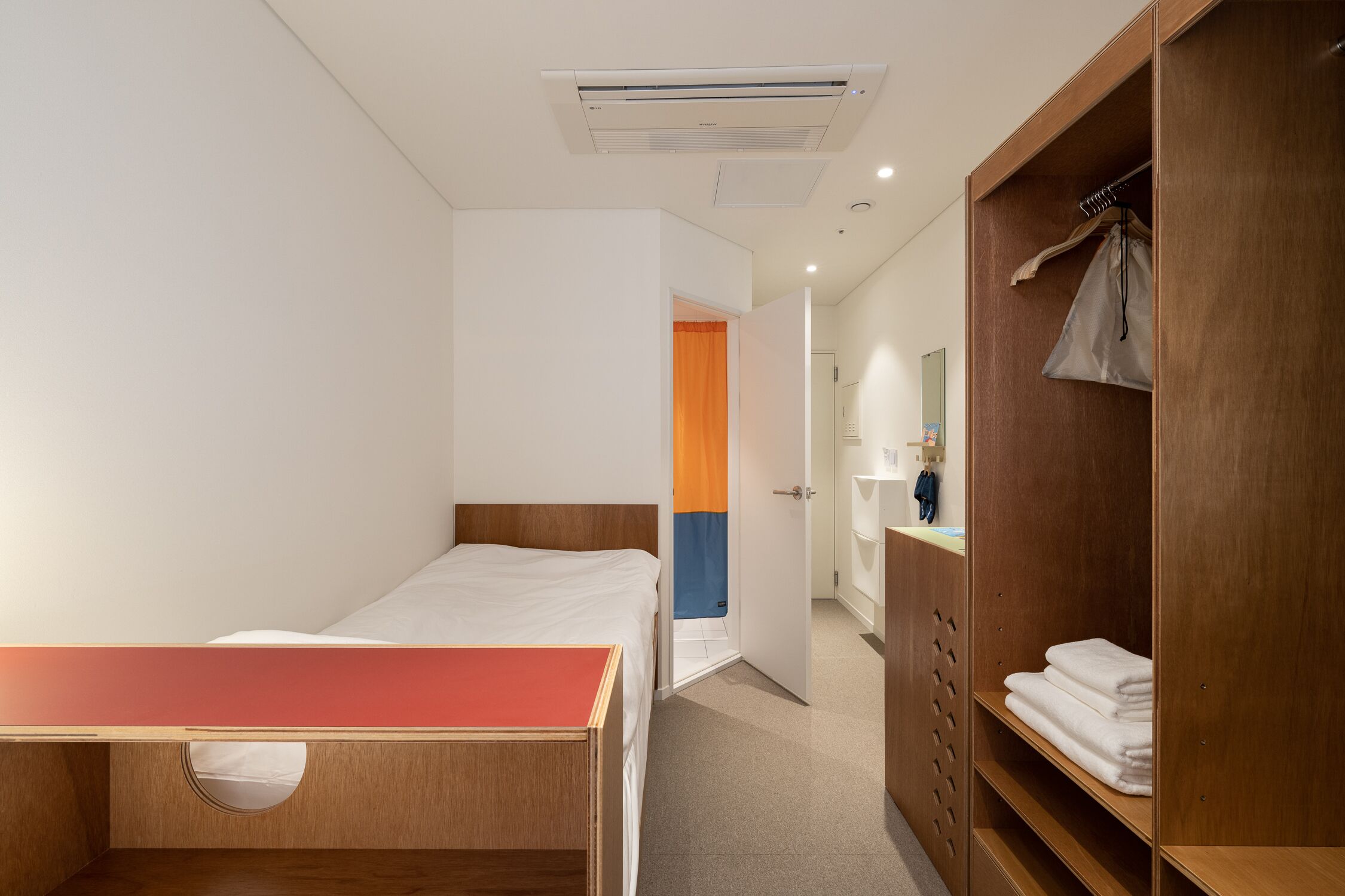 A hotel room with a single bed, a wooden desk, a wardrobe, and a bathroom visible through an open door.