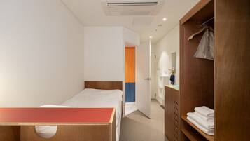 A hotel room with a single bed, a wooden desk, a wardrobe, and a bathroom visible through an open door.