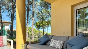 Un espace extérieur lumineux, aménagé avec un canapé gris, des coussins à motifs et des vases en verre transparent posés sur une nappe à rayures.