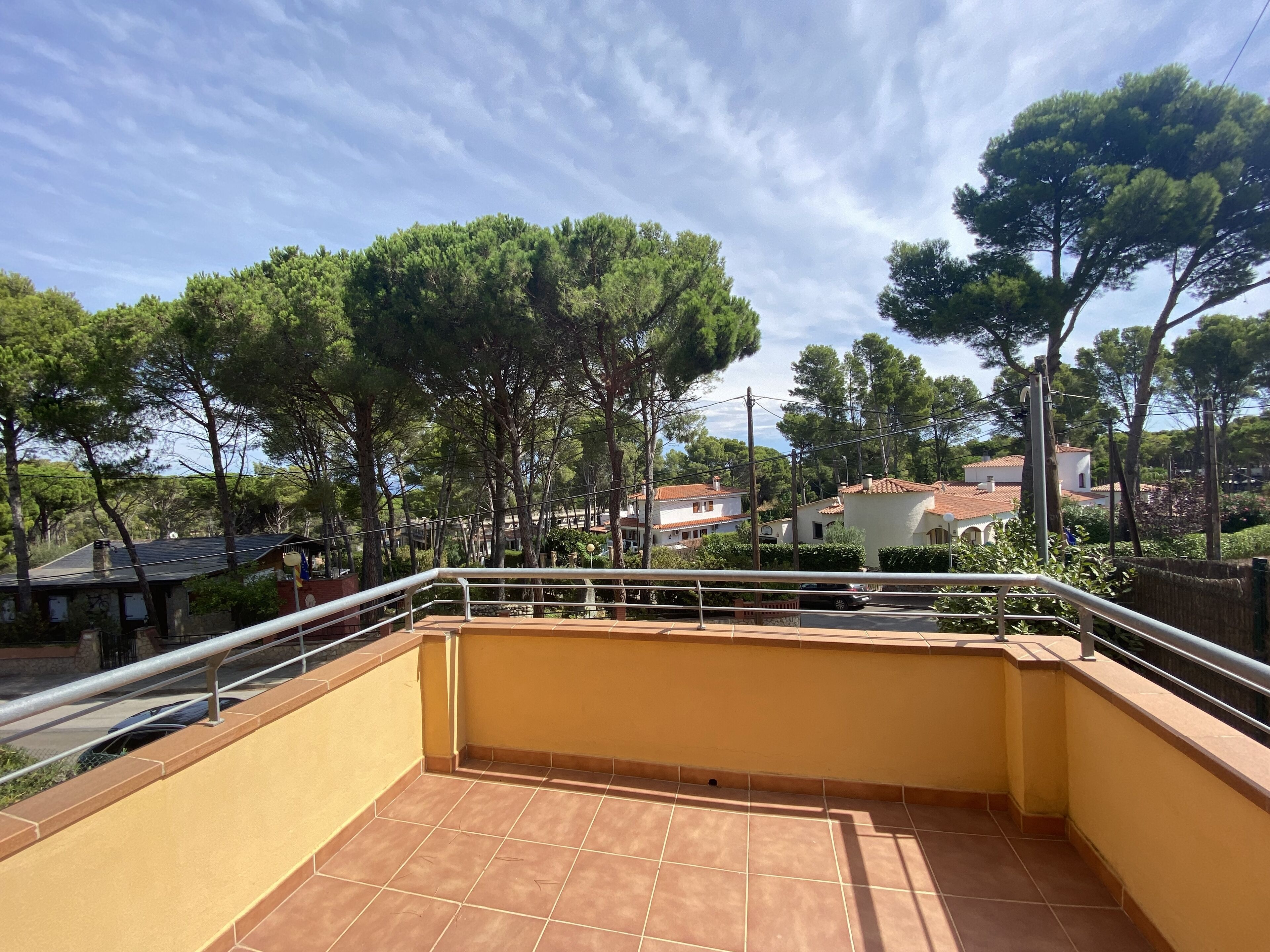 A balcony with a tiled floor, metal railing, and a view of trees and houses in the background.